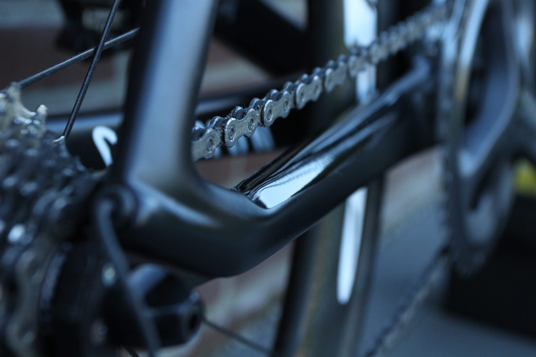Transparante PPF-beschermfolie op de liggende achtervork van een zwarte fiets, tegen kettingslag